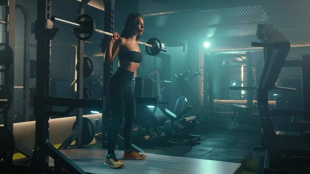 A young and dedicated sportswoman squatting with a barbell, working on her lower body strength in a modern, well-lit gym full of various equipment. Camera 8K RAW. 