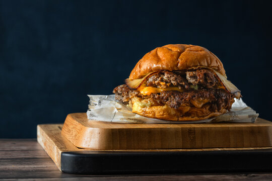 Deliciosa hamburguesa con doble carne aplastada, doble queso sobre tabla de cocina en una mesa de madera r&uacute;stica en un fondo azul