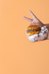 Mano de niña sosteniendo una hamburguesa con fondo naranja en vertical para redes sociales con...
