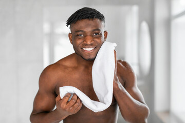 black millennial man wipes face with towel in modern bathroom