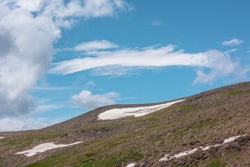 Scenic alpine view to stony hill with snowfield in sunlight. Minimalist landscape with rocky hills...