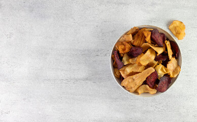 A bowl of vegetable organic chips made from beets, carrots and celery root on a gray background. Top view. Copy space