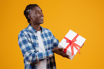 Delighted young black man holding white gift box with red ribbon - obrazy, fototapety, plakaty