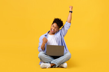 Exuberant black male student celebrating with laptop on yellow background