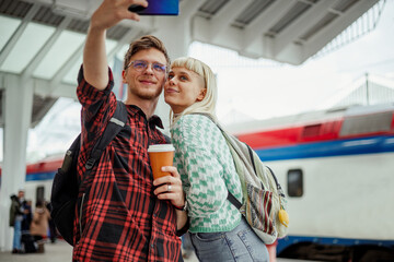 Couple taking selfie with a phone and drinking coffee on a train station