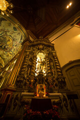 Altar de igreja católica com imagens de santos, teto alto e luz amarelada. 