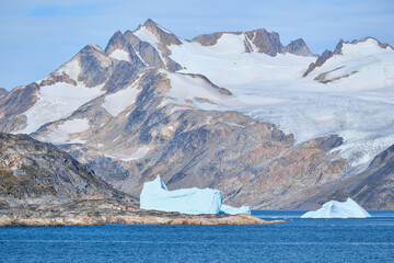 Icebergs float beside massive, glaciated mountain.  East Greenla