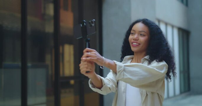 Woman records herself using a gimbal stabilizer amidst the charming setting of a decorated alley.