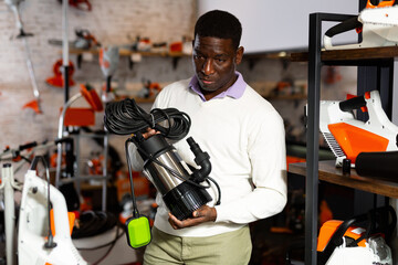 African-american man standing in salesroom of gardening tools store with drainline pump in hands.
