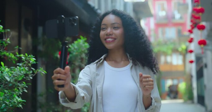 Woman records herself using a gimbal stabilizer amidst the charming setting of a decorated alley.