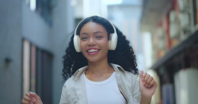 Serene young woman smiling with headphones on, enjoying music in a calm city environment.