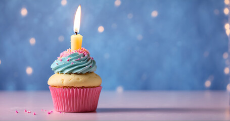 Un petit cup cake en forme de gâteau d'anniversaire avec de la crème et une bougie allumée sur un fond bleu et rose dans une ambiance festive
