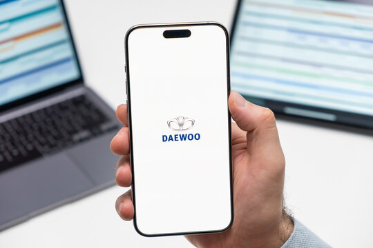 PRAGUE, CZECHIA - FEBRUARY, 2024: Daewoo automobile logo on the screen of smartphone in mans hand and laptop on the background 
