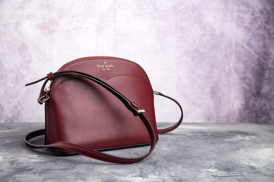 Kate Spade New York women's crimson leather handbag on a gray background. Space for text.