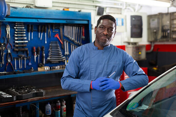 Professional man car mechanician standing near repairable car in auto repair shop