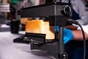 Electric Cheese Melter Slicing through a Wheel of Raclette Cheese