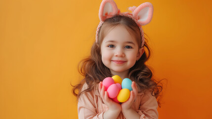 Fototapeta na wymiar Easter joy: girl with bunny ears holding colored eggs on orange background