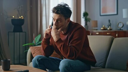 Unhappy man worried call sitting couch close up. Upset guy talking mobile phone