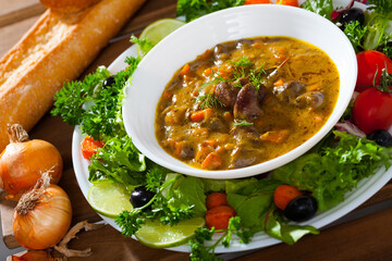 Tasty goulash with chicken hearts and vegetables served with greens and fresh baguette..
