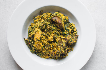 Nigerian egusi soup with fish and beef in a white plate, egusi vegetable soup in a large dinner plate, traditional egusi soup in a white dish