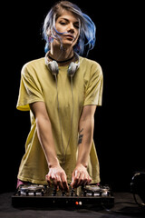 Girl wearing headphones is focused on mixing music on a soundboard. Female DJ with blue hair and...