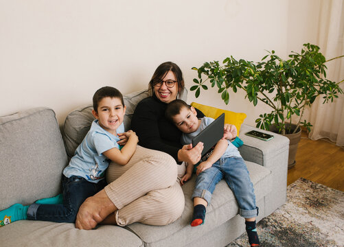 Happy smiling mother with disability sitting on couch with her children and looking at tablet together.
