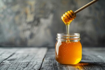 Honey flows from a wooden dipper into a jar on a rustic grey surface - obrazy, fototapety, plakaty