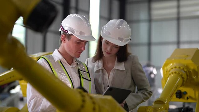 Business engineers meet and check control heavy machine robot arm. Diverse Team of Industrial Robotics Engineers Gathered Around machine. Professional Machinery Operator Use Industrial Digital Tablet.