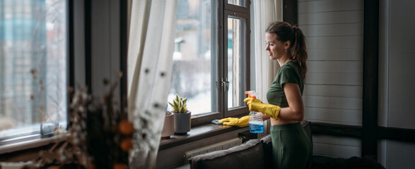 Weekend homework. Young pretty woman washes window in cozy living room at home.