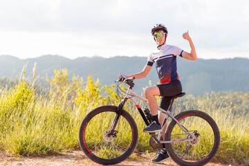 Fototapeta premium Brazilian cyclist standing with his bike and giving a thumbs up sign with his hand. He is happy and smiling while looking at the camera. In the background, landscapes with hills.