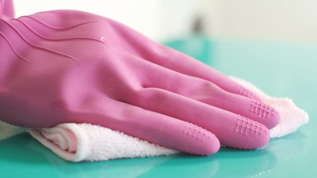 Female hand in pink glove wipes surface with rag.