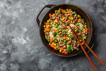 Top view of Asian street food with wok cooked turkey soba noodles corn peas green beans and carrots on a gray background served with chopsticks