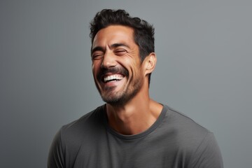 Portrait of a handsome young man laughing and looking up against grey background - obrazy, fototapety, plakaty