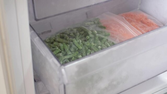 Female hand pulls out drawer in refrigerator with packages of frozen food.