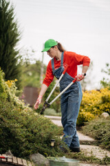 A female gardener wearing gloves performs repair work and trims bushes. Garden work in spring
