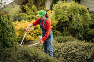 A female gardener wearing gloves performs repair work and trims bushes. Garden work in spring