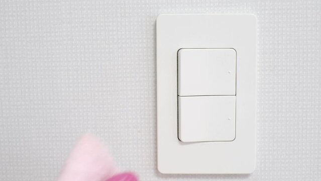 Female hand in rubber gloves wipes light switch in the room with a pink rag close-up.