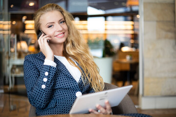 Portrait of a young woman talking on the phone and using a digital tablet on a break