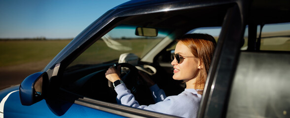 young woman driver driving a car in sunglasses during the day.