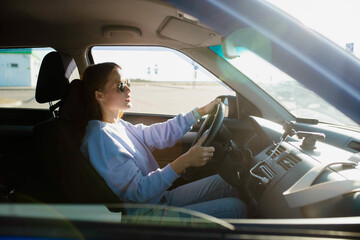 young woman driver driving a car in sunglasses during the day.