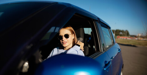 young woman driver driving a car in sunglasses during the day.