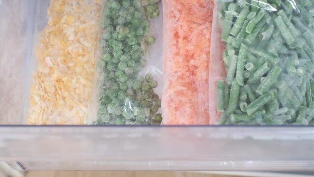 Female hand folds plastic bags with chopped vegetables into the freezer, top view close-up.