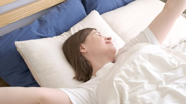 Portrait of beautiful young woman who wakes up and stretches on bed, side view.