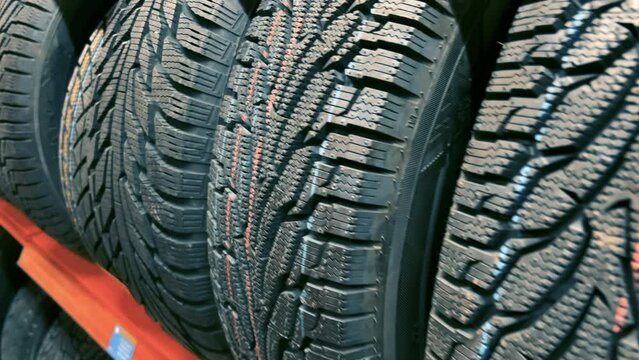 Close-up view of new winter tires on display at a car store. The tires are stacked on a shelf and have a variety of features, including aggressive tread patterns for traction in snow and ice