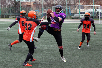 Three American football players attack another player with the ball