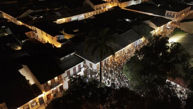 Aerial shot drone orbits crossroads of plaza at night with large crowd