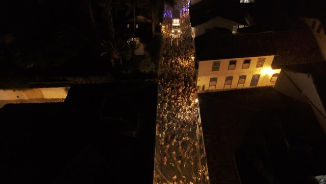 Aerial shot drone flies low over street at night with bloco during Carnaval in Paraty
