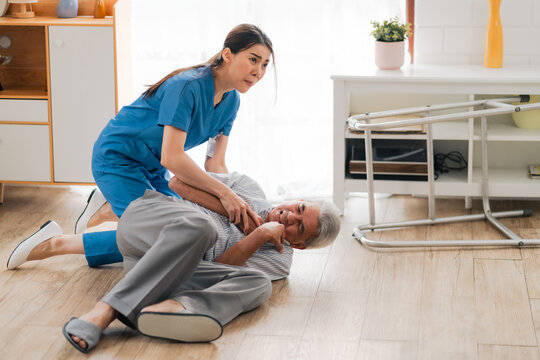 senior patient falling on the ground floor at home, Asian caregiver helping elderly older male from accident after doing physical therapy then rescued by attractive therapist nurse, health insurance