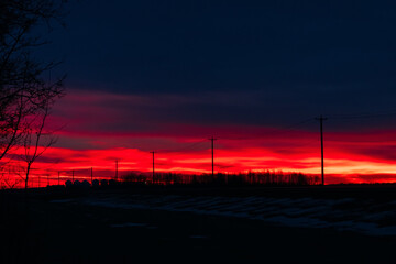 Fototapeta premium Dramatic red sunrise and the calm highway in prairies in winter.