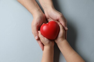 Mother and her child holding red decorative heart on gray background, top view